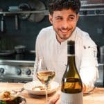portrait de Quentin Maufrais avec un verre de vin et une bouteille de Versant Viognier des Vignobles de Foncalieu